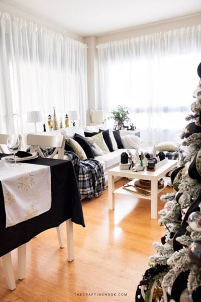 Bright Christmas living room with white sectional sofa, black and gold pillows, plaid blankets, and black and white Christmas decorations.