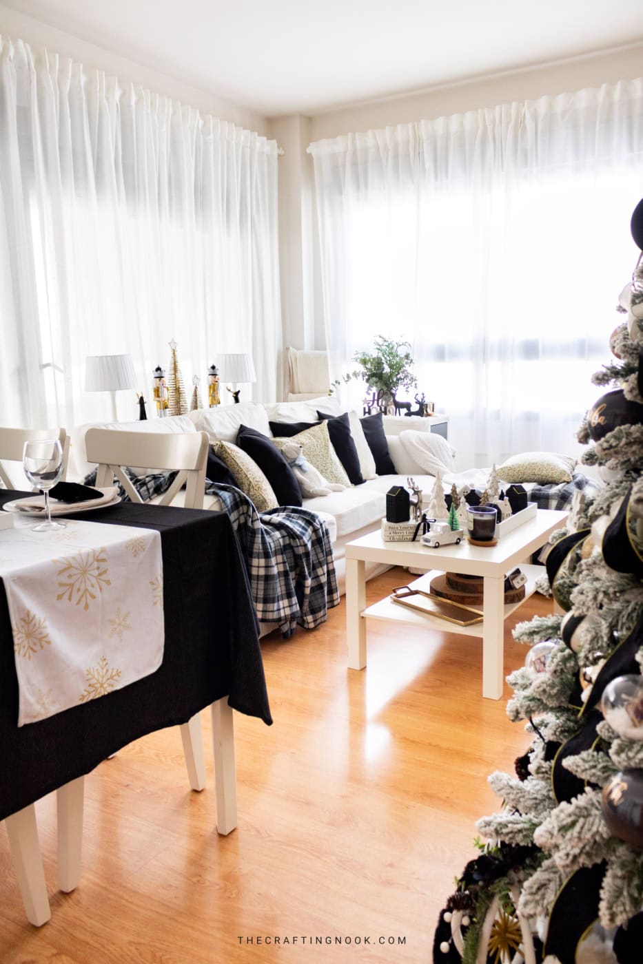 Bright Christmas living room with white sectional sofa, black and gold pillows, plaid blankets, and black and white Christmas decorations.