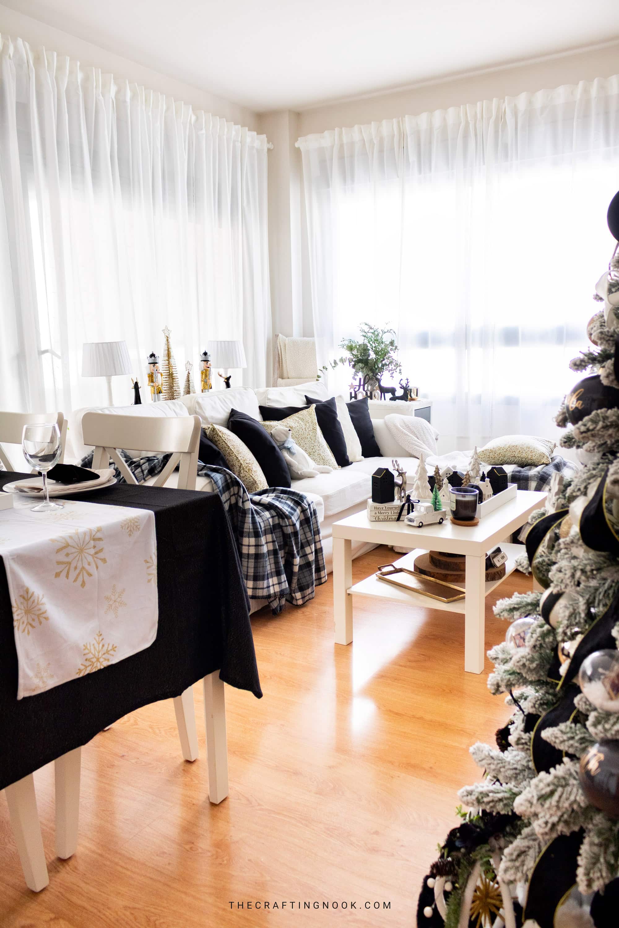Bright Christmas living room with white sectional sofa, black and gold pillows, plaid blankets, and black and white Christmas decorations.
