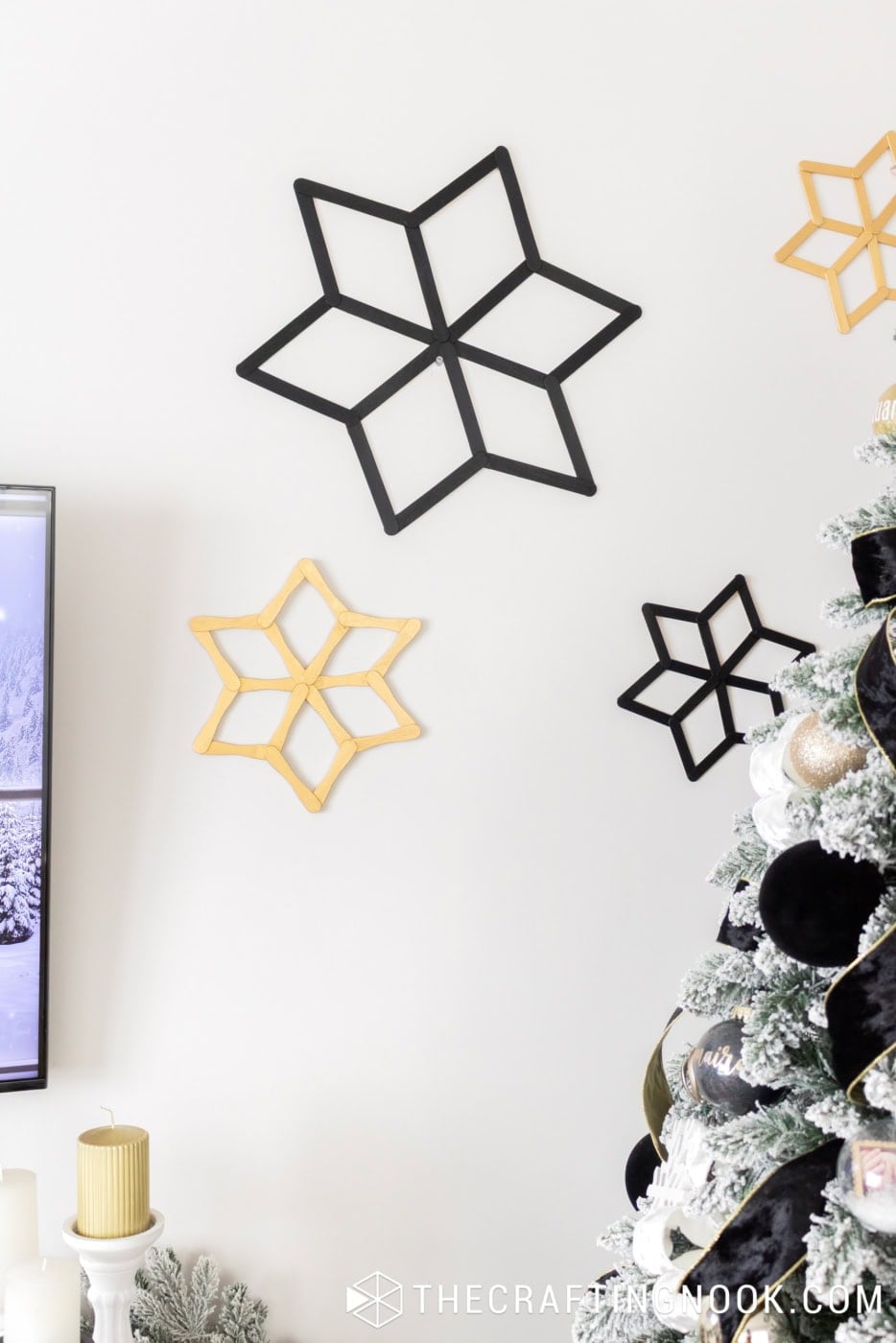 Large black and smaller gold popsicle stick snowflakes displayed on the wall beside a flocked Christmas tree.