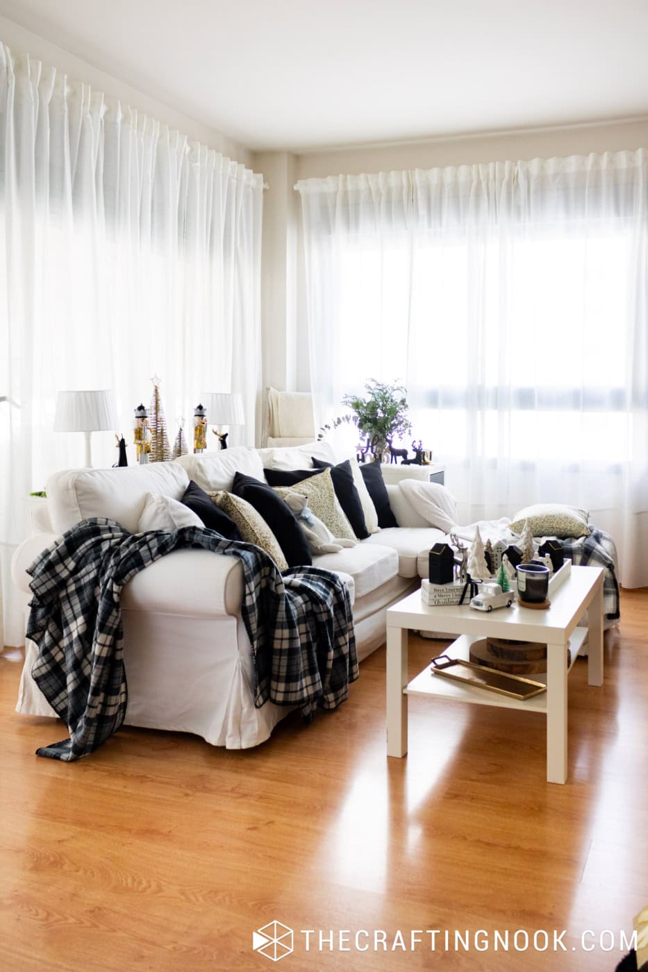 White sectional sofa decorated with black pillows, gold-patterned cushions, plaid throws, and Christmas accents.
