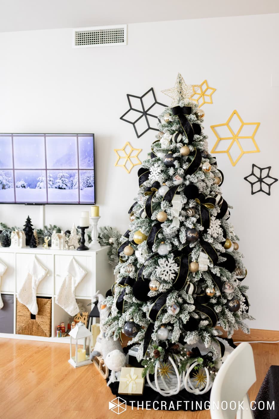 Full flocked Christmas tree decorated with black velvet ribbons, white snowflakes and gold ornaments beside a white Christmas mantel display.