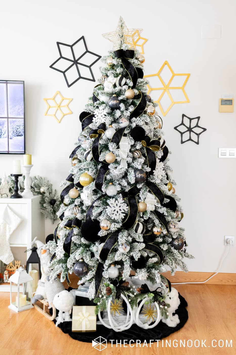 Flocked Christmas tree decorated with black, white, and gold ornaments, surrounded by handmade popsicle stick snowflakes on the wall.