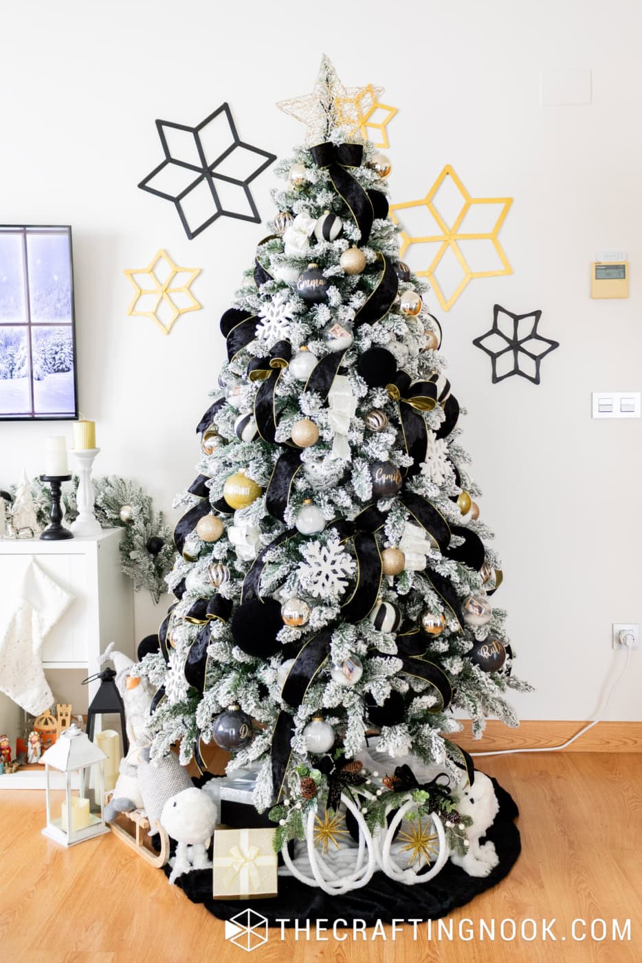 Elegant black, white and gold Christmas tree with snowy branches, velvet ribbons, personalized ornaments, white snowflakes and handmade hoop decorations at the base.