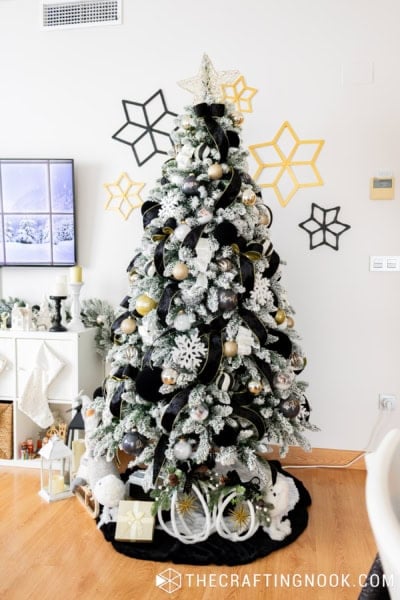 Elegant black, white and gold Christmas tree with velvet ribbons, gold ornaments and snowy flocked branches in a decorated living room.