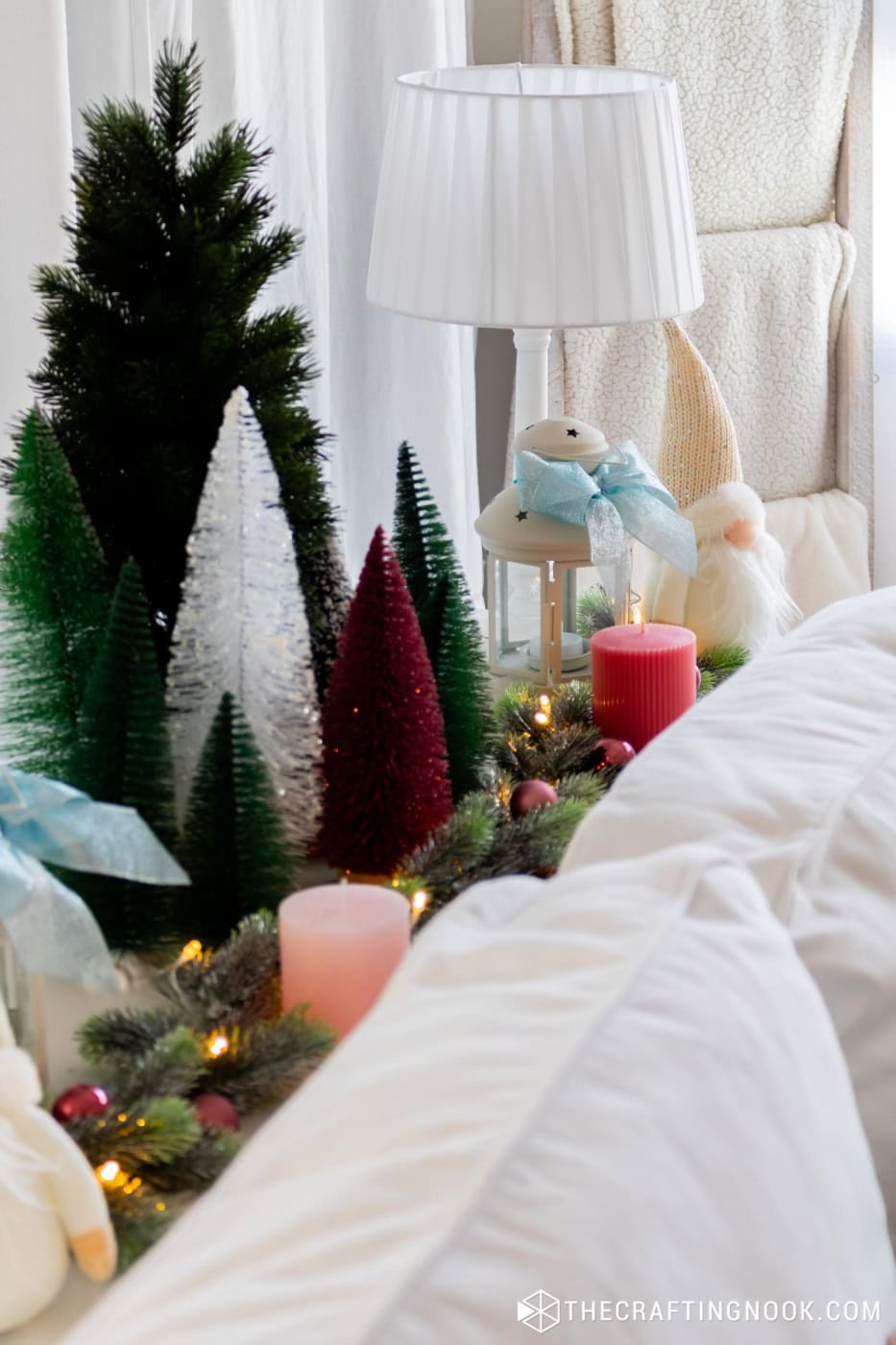 Close view of bottle brush trees, a white lantern with a blue bow, candles and a gnome behind the sofa