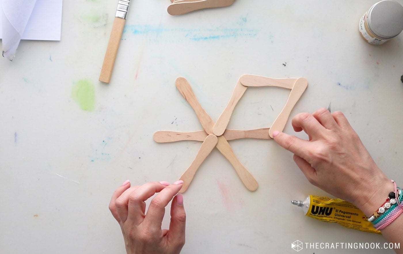 Connecting popsicle sticks to form the first diamond-shaped point of a wooden Christmas snowflake.