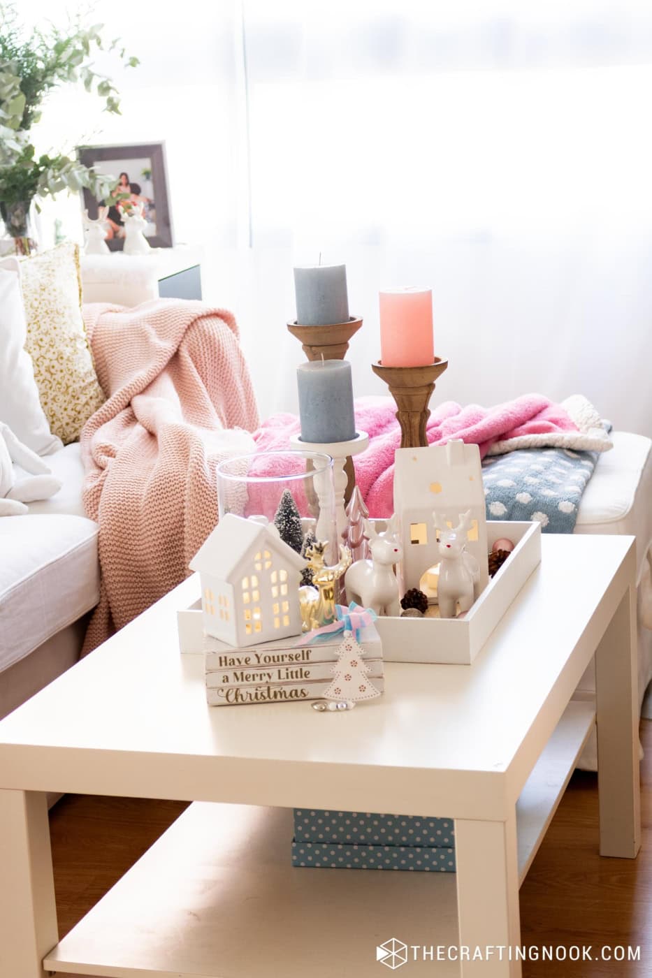 Coffee table with a white tray of lit houses, reindeer, candles and a Merry Little Christmas book stack