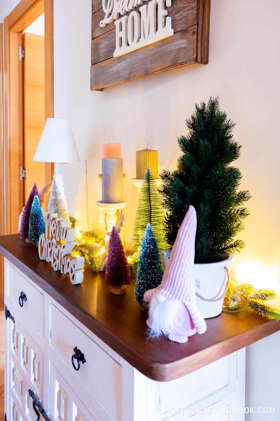 Side view of a white console with a pink gnome, a small tree, bottle brush trees and warm lights