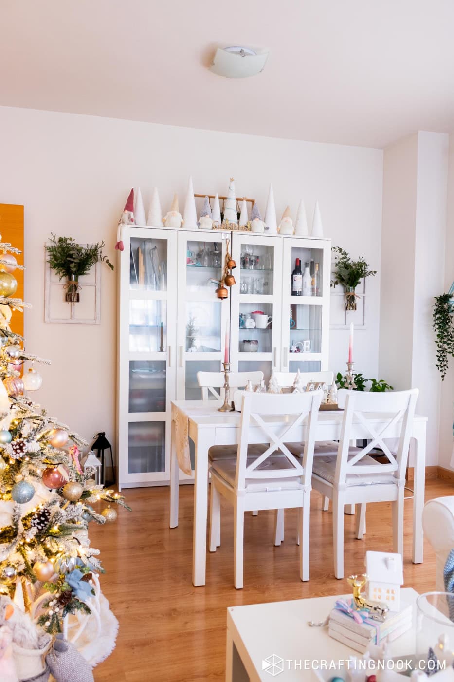 White hutch decorated with white cone trees and gnomes, with a dining table and the Christmas tree beside it