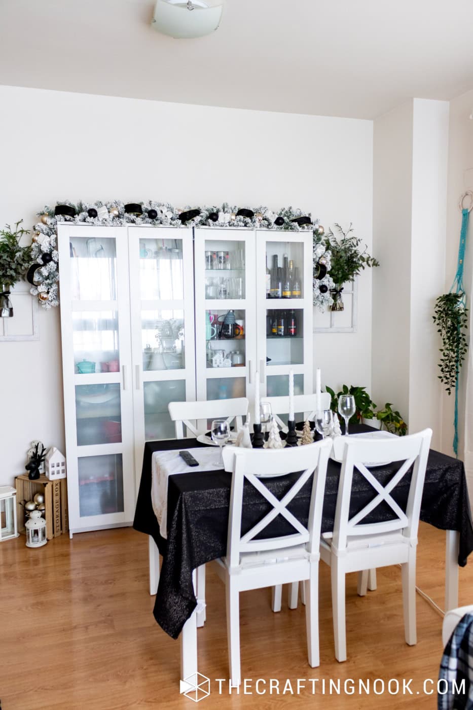 White glass-front dining room cabinets decorated with flocked Christmas garland, black velvet ribbon, and gold ornaments.

