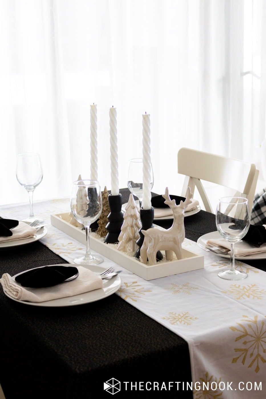 Christmas dining table set with white plates, black star decorations, twisted white candles, and a handmade snowy centerpiece.
