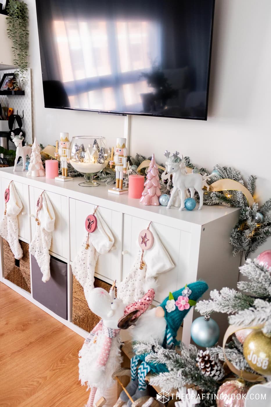 Angled view of a Christmas TV console with nutcrackers, a garland, stockings and gnomes by the tree