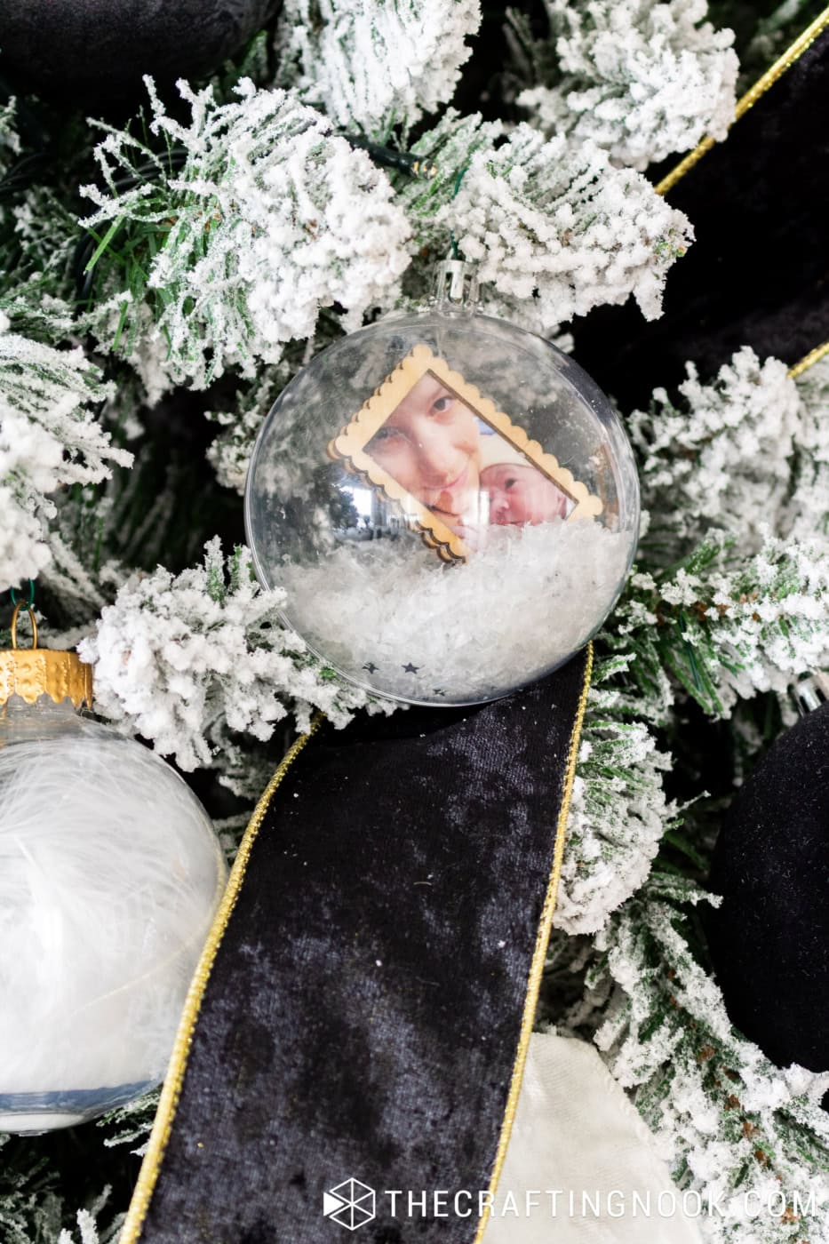Clear Christmas snow globe ornament filled with artificial snow and a special family photograph, hanging beside black velvet ribbon.