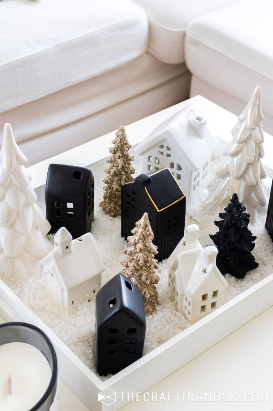 Handmade Christmas village centerpiece with black and white ceramic houses, gold glitter trees, white ceramic trees, and faux snow.
