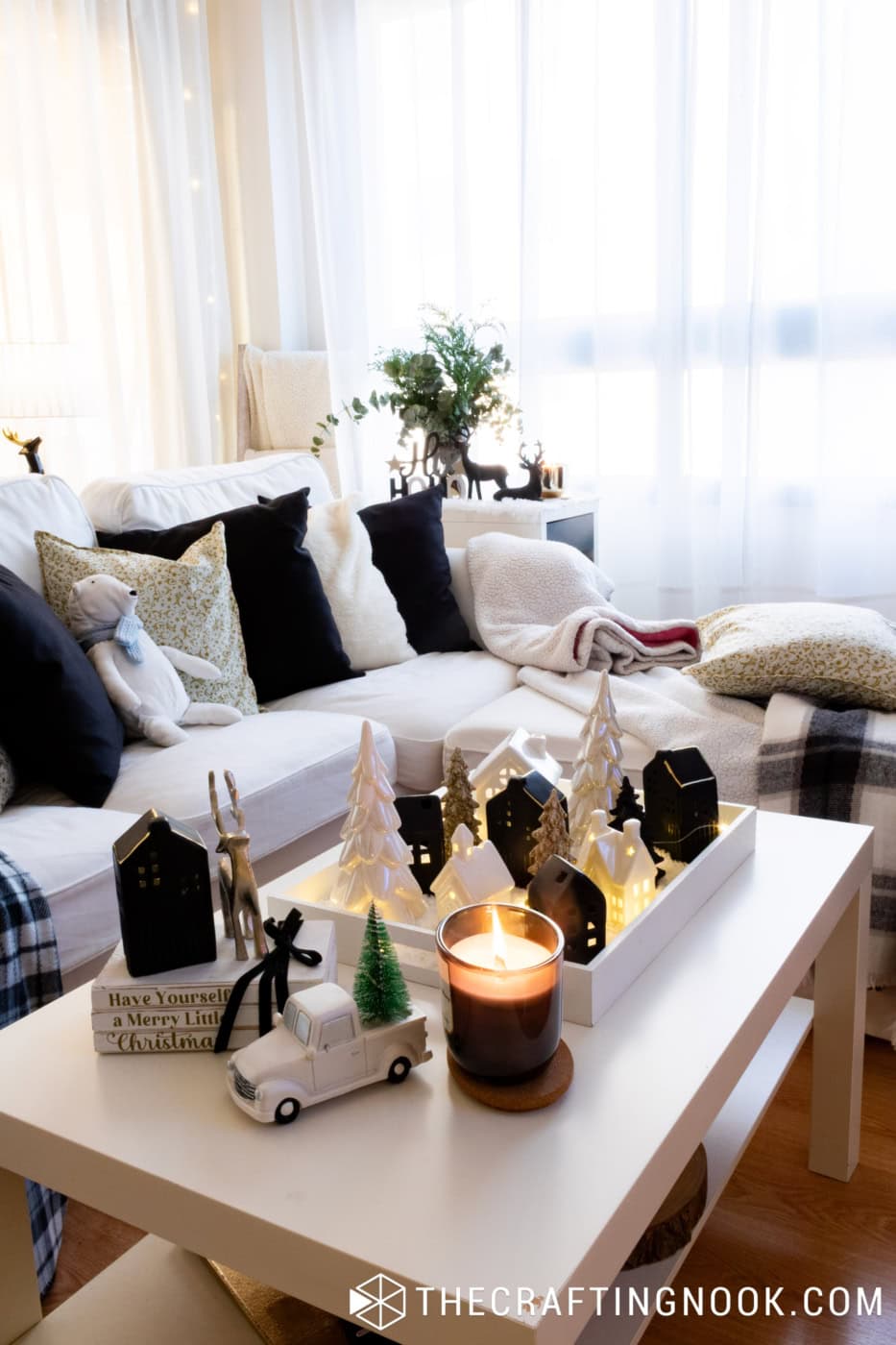 Illuminated black and white Christmas village centerpiece on a white coffee table with glowing ceramic houses and a lit candle.

