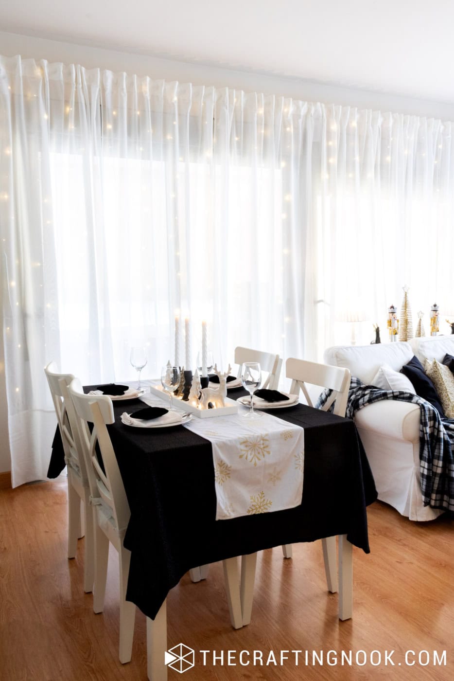 Black, white, and gold Christmas dining room with a black tablecloth, white chairs, gold snowflake runner, and festive table centerpiece.
