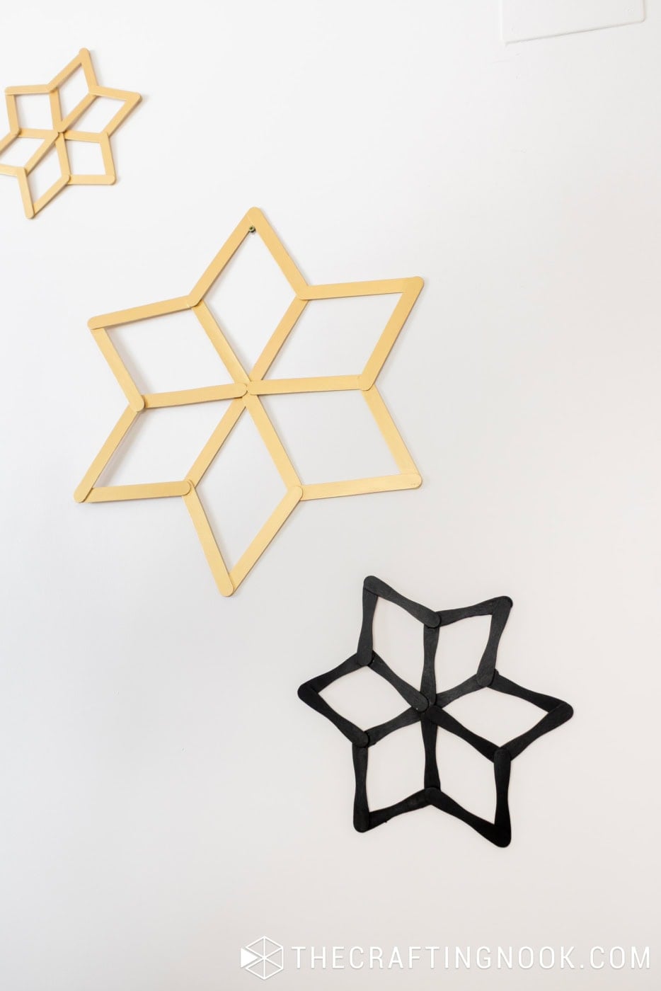 Large metallic gold and smaller black popsicle stick snowflakes hanging together on a white wall.