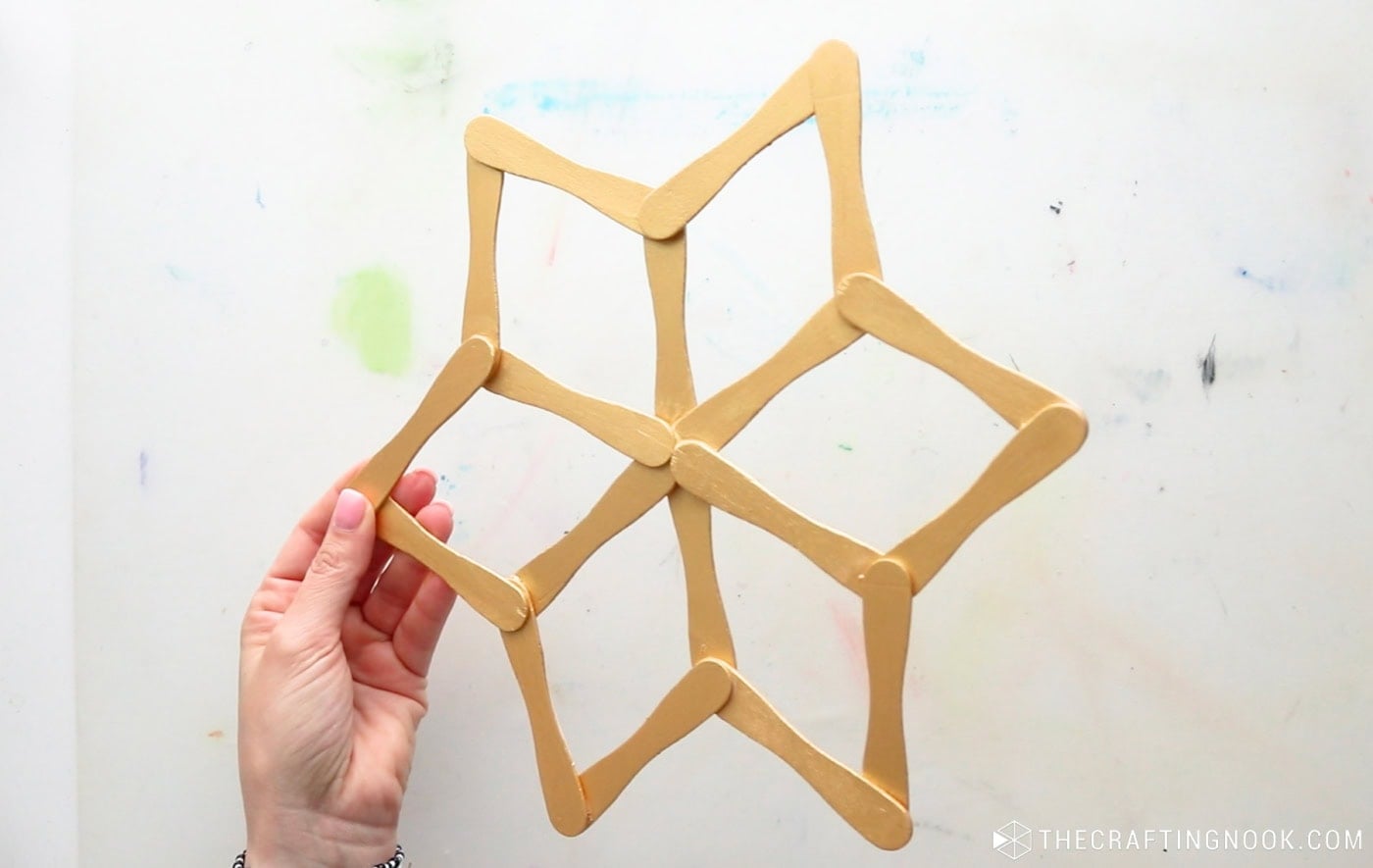 Holding a finished gold popsicle stick snowflake made with 18 wooden craft sticks.