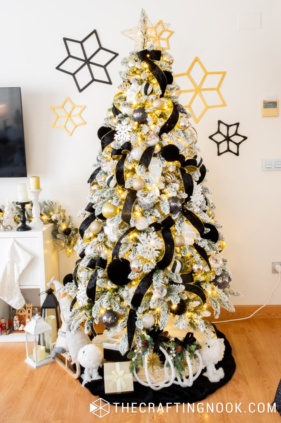 Snowy Christmas tree glowing with warm white lights, black velvet ribbons and shimmering gold decorations.