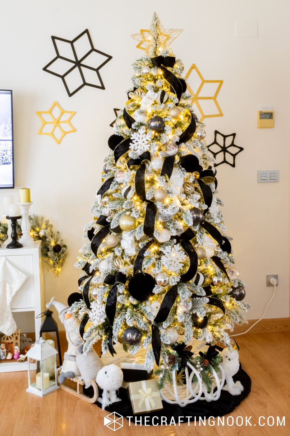 Elegant flocked Christmas tree decorated with black velvet ribbons, white snowflakes, gold ornaments, and black and gold star wall decorations.
