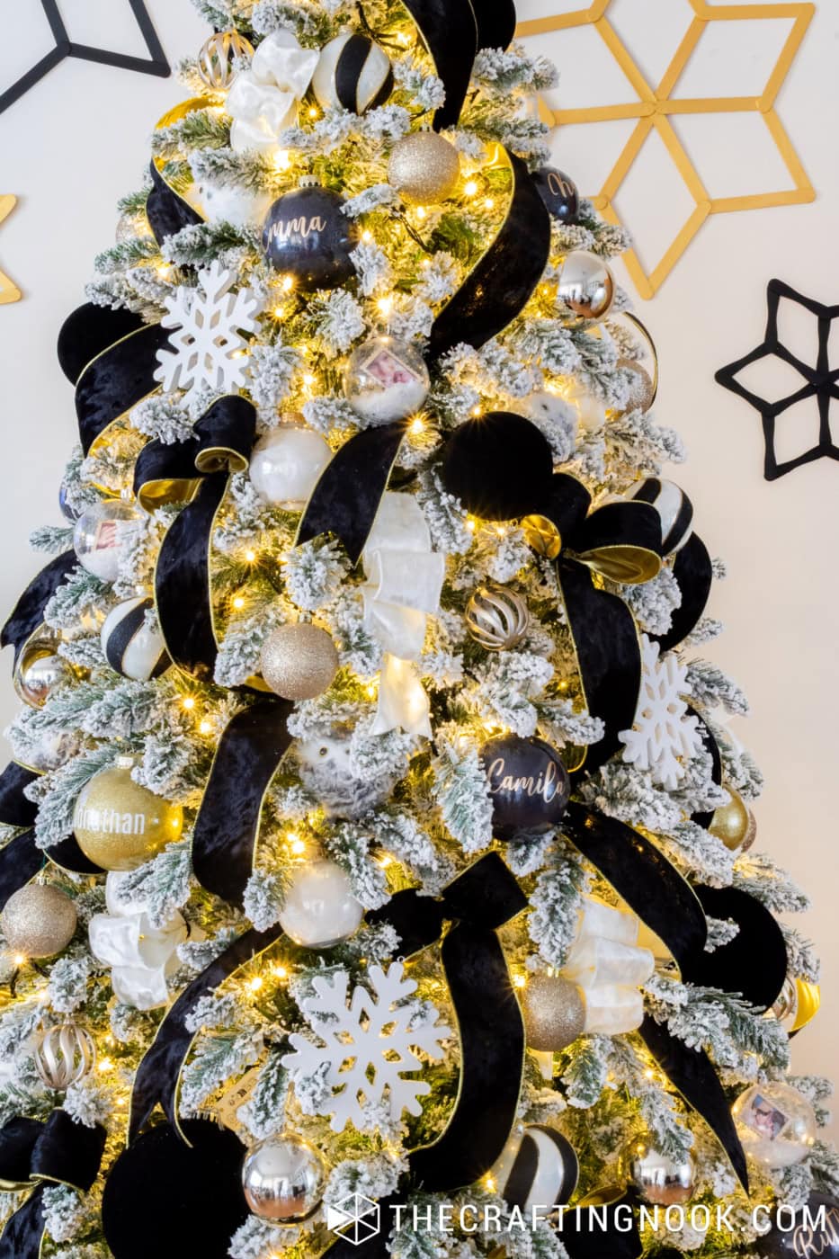 Black glitter Christmas ornament personalized with Emma in white vinyl lettering on a flocked Christmas tree.