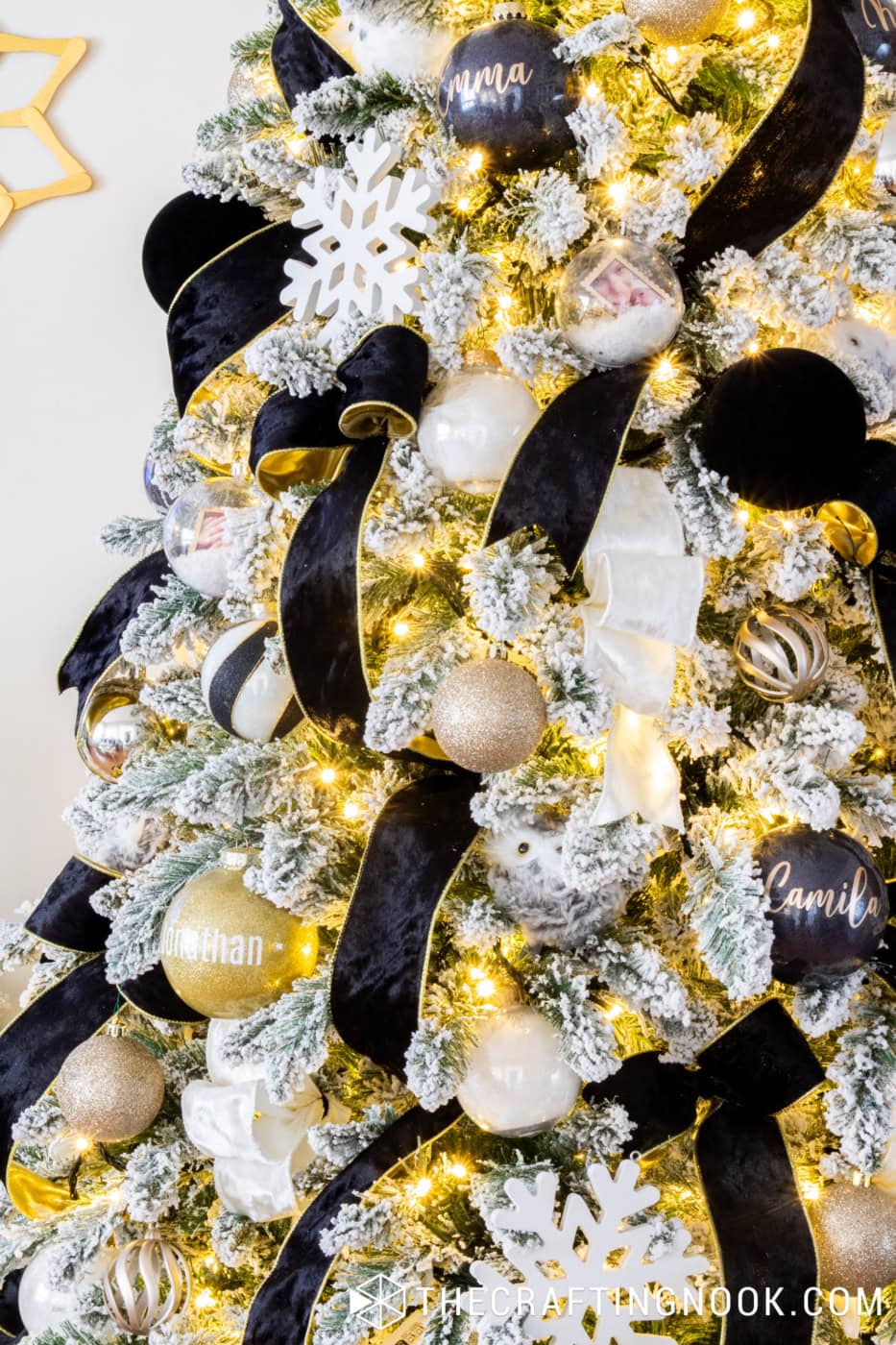 Black, white and gold Christmas tree ornaments in different textures and finishes, with velvet ribbons and warm white lights.