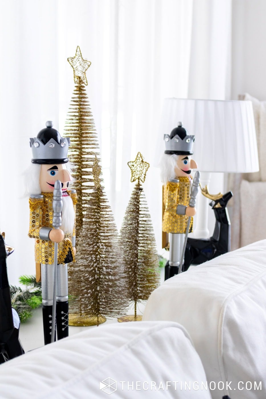 Two gold and silver Christmas nutcrackers displayed with gold bottle-brush trees and black reindeer behind a white sofa.
