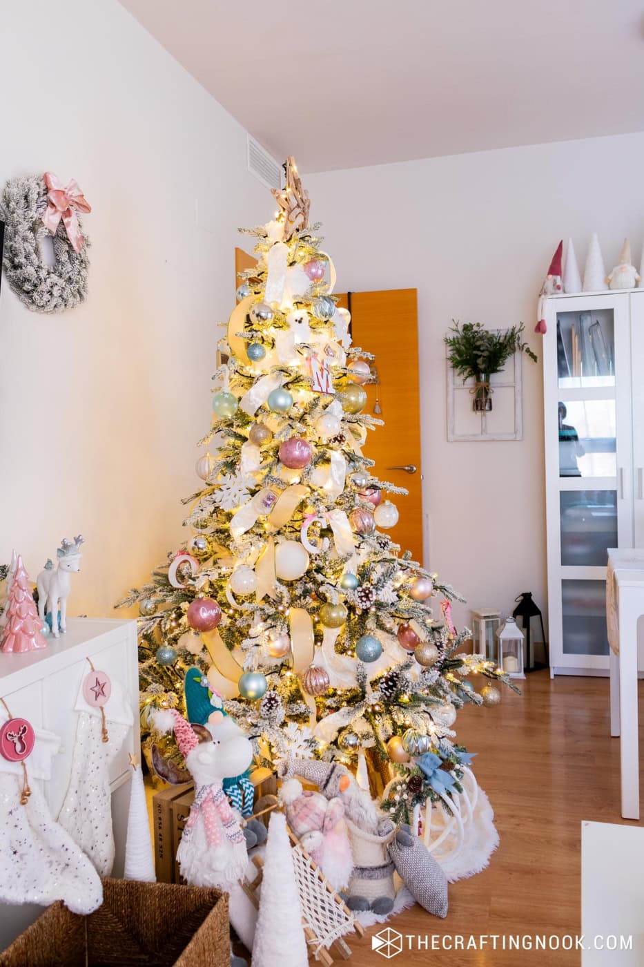 Full flocked Christmas tree with pink, blue and gold ornaments, ribbon and a wooden star topper