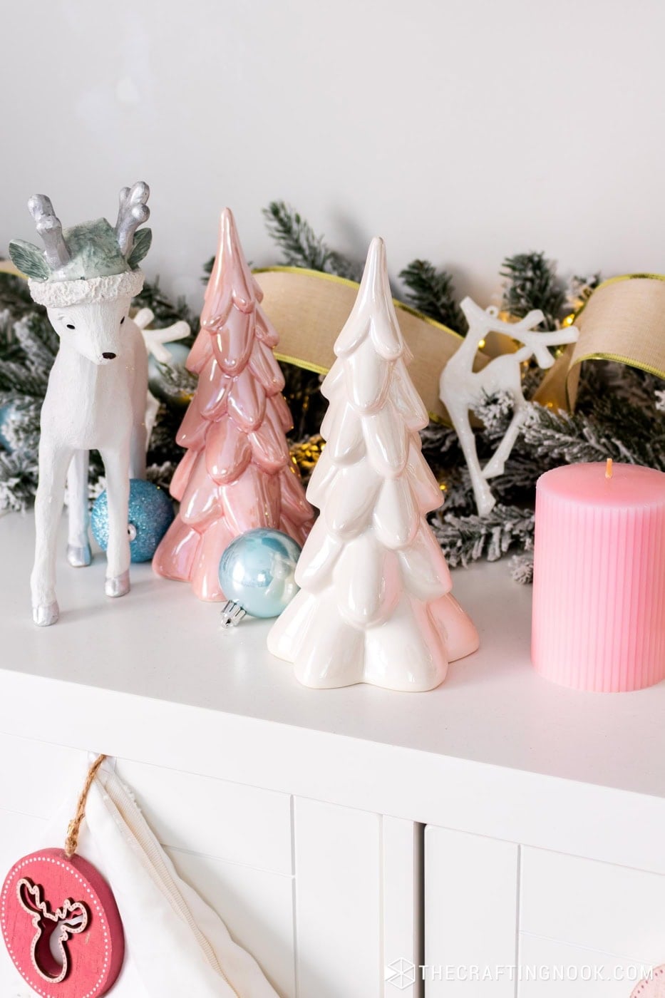Pink and white pearly ceramic Christmas trees next to a white reindeer, blue ornaments and a pink candle