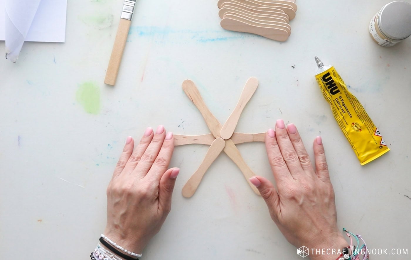 Six wooden popsicle sticks overlapping at the center to create the base of a six-pointed snowflake.