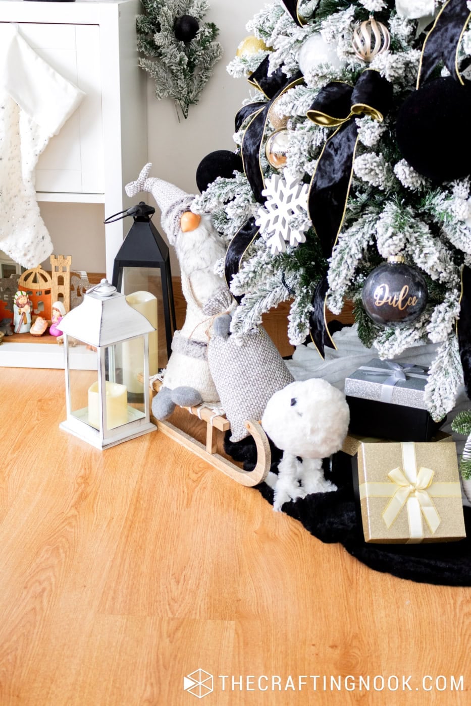 Close-up of flocked Christmas tree with wide black velvet ribbons, gold ornaments, white snowflakes, and warm white Christmas lights.
