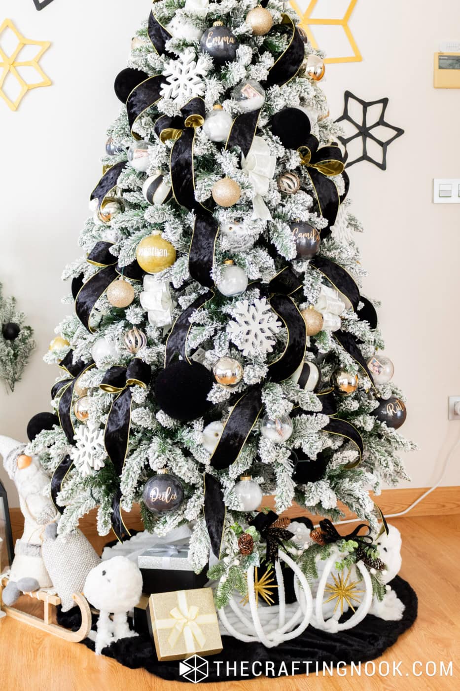 Black, white and gold Christmas tree with handmade white hoop decorations, greenery, gifts and a black tree skirt at the base.