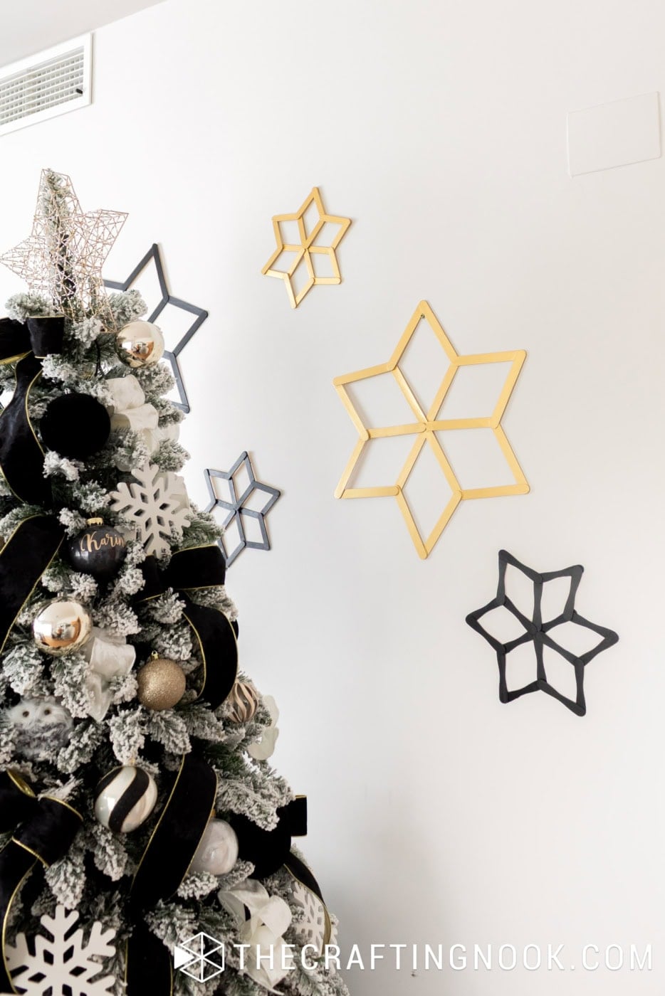 Black and gold popsicle stick snowflakes arranged beside a Christmas tree decorated with black velvet ribbon and gold ornaments.