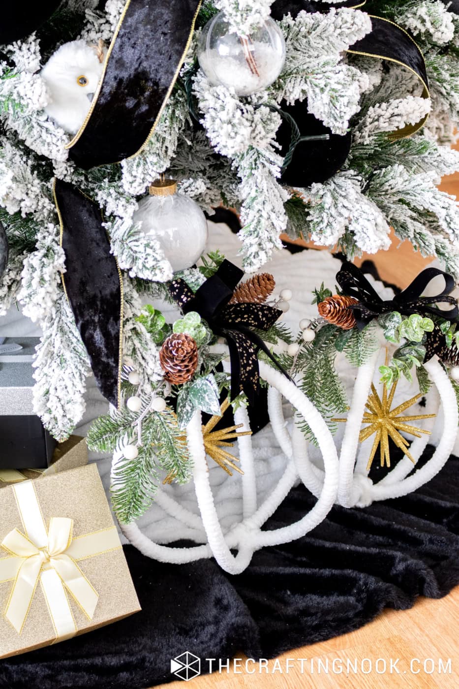 Base of a black, white, and gold Christmas tree decorated with a winter gnome on a wooden sled, white lanterns, fluffy animals, and wrapped gifts.
