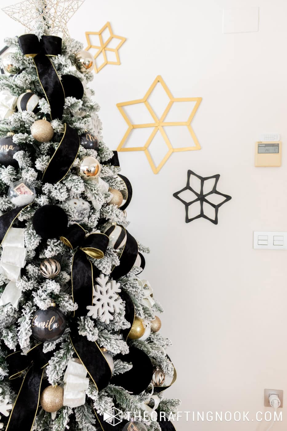 Handmade black and gold geometric popsicle stick snowflakes decorating the wall beside a flocked Christmas tree.