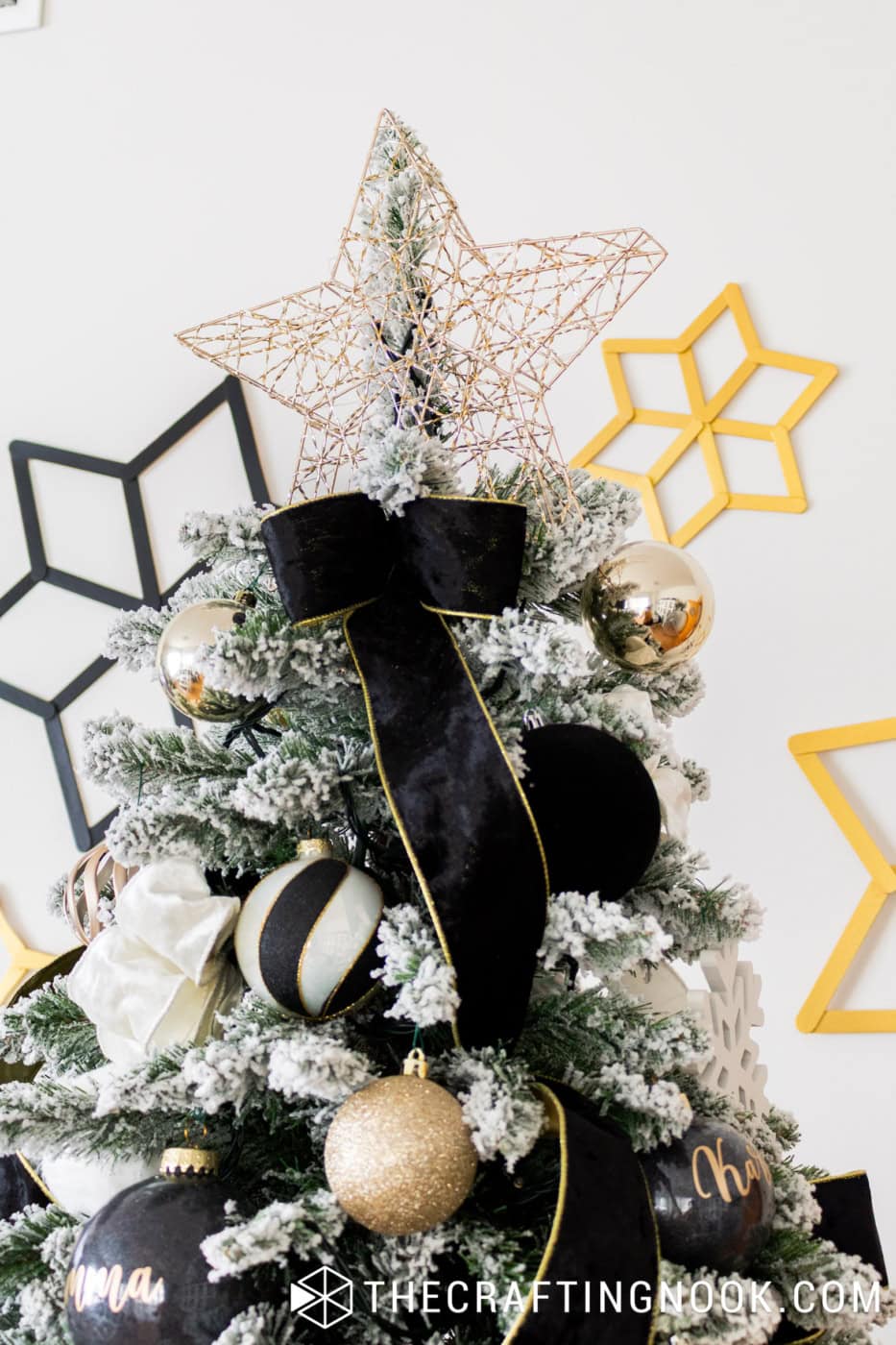 Openwork gold star Christmas tree topper above black velvet ribbon, gold baubles and snow-covered branches.